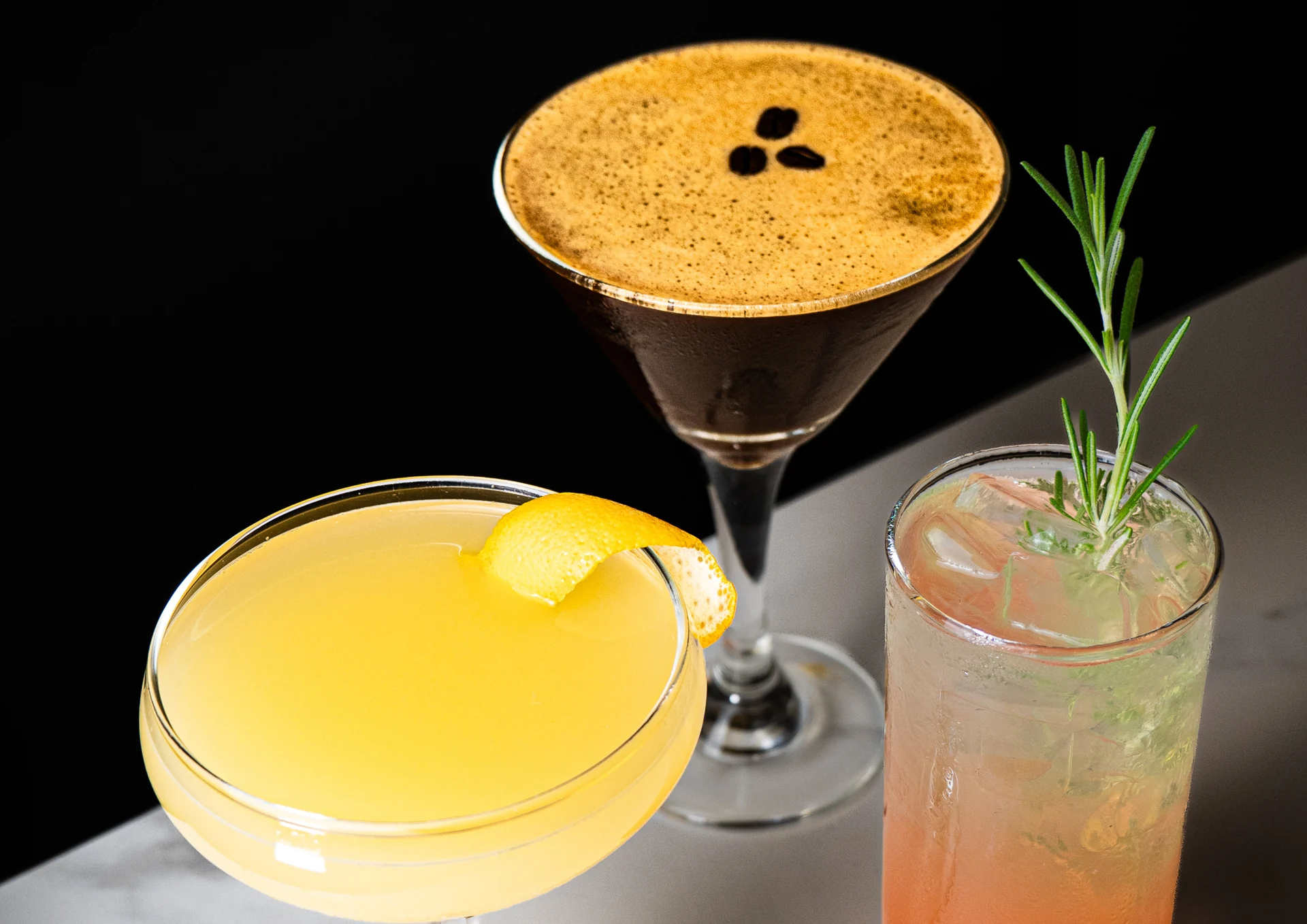 Three cocktails with citrus, rosemary and coffee garnish